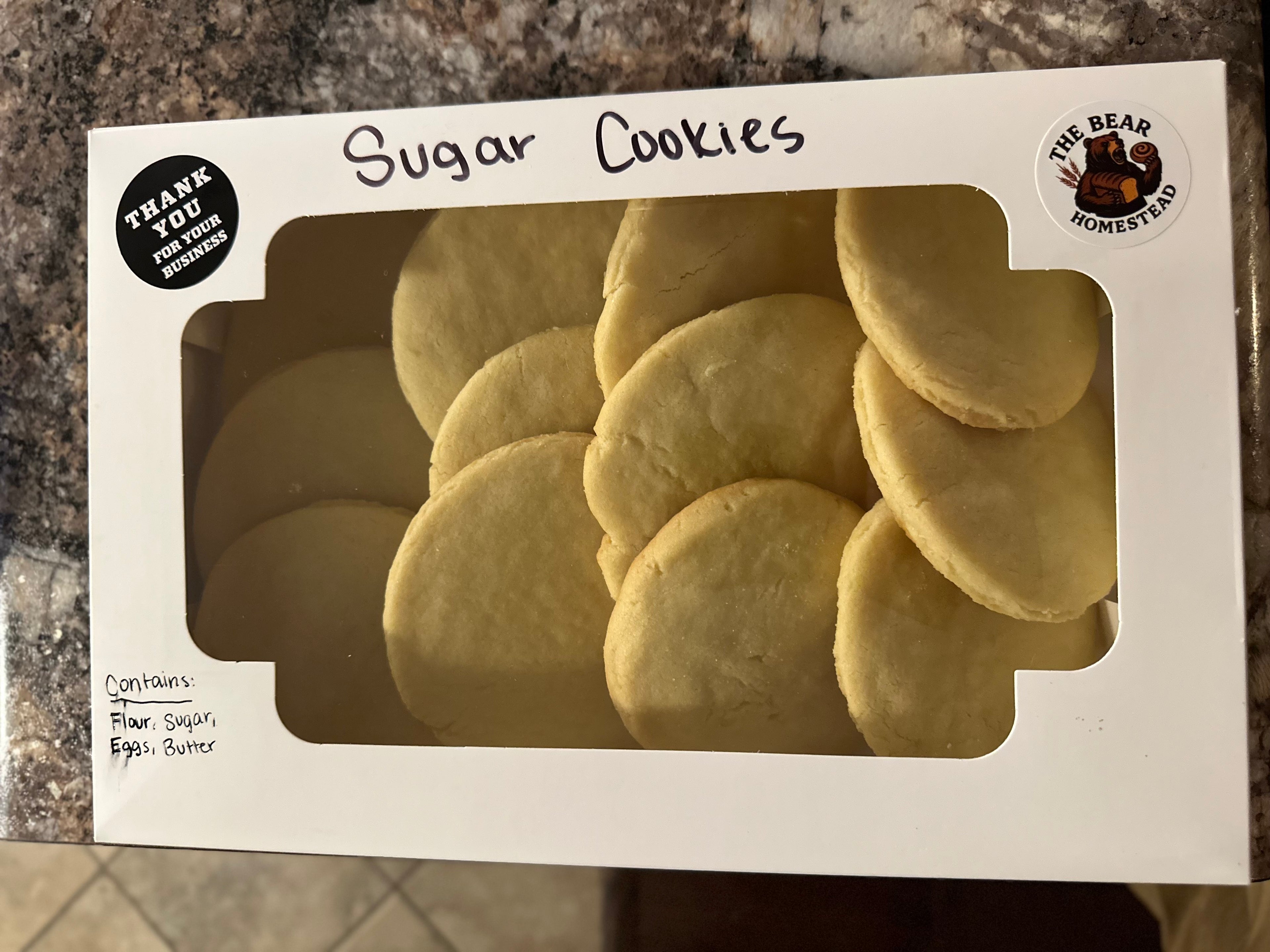 Box of sugar cookies with a clear window showing the cookies inside, on a countertop.